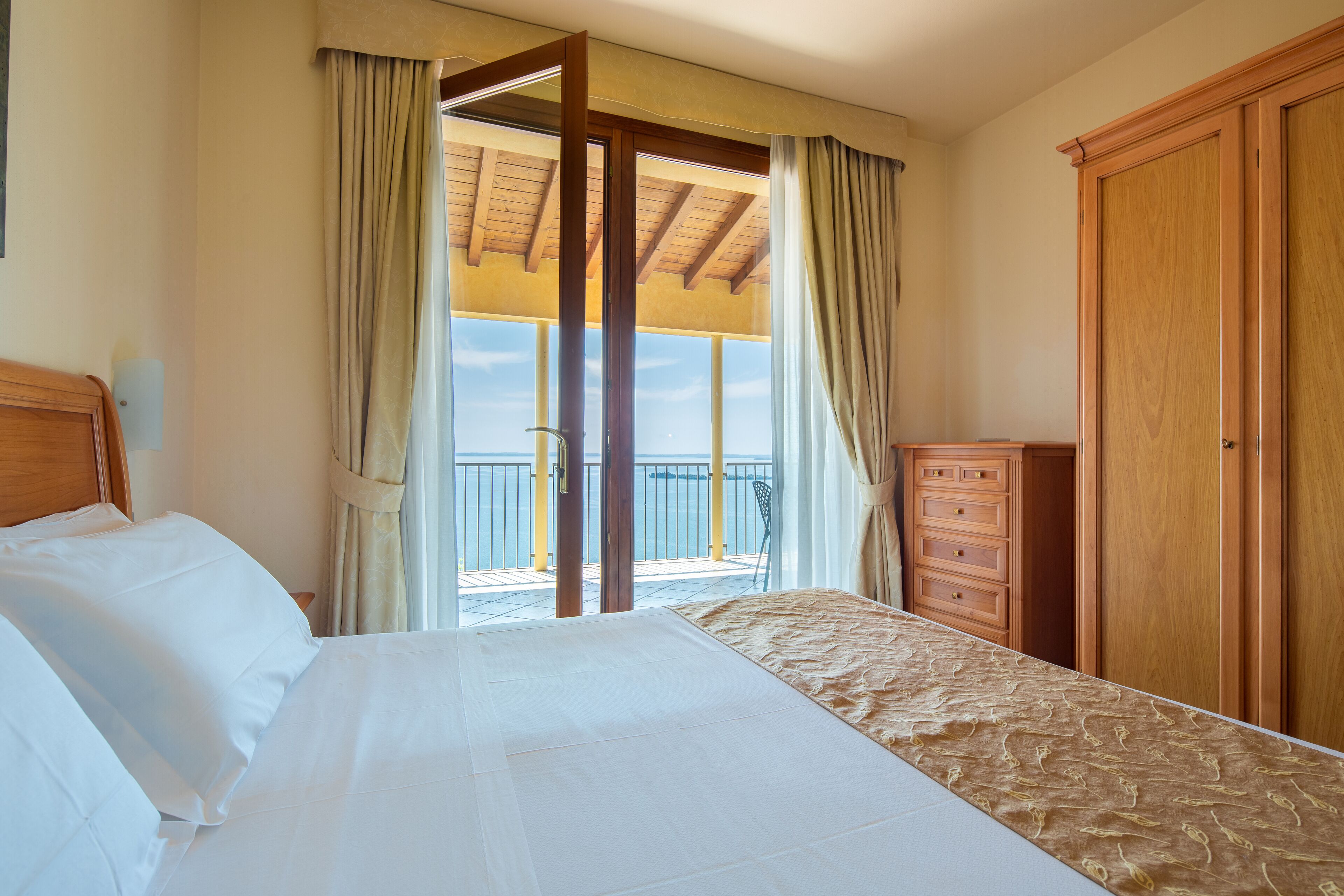 Une chambre à coucher avec un lit, une armoire en bois et un balcon avec des rideaux.