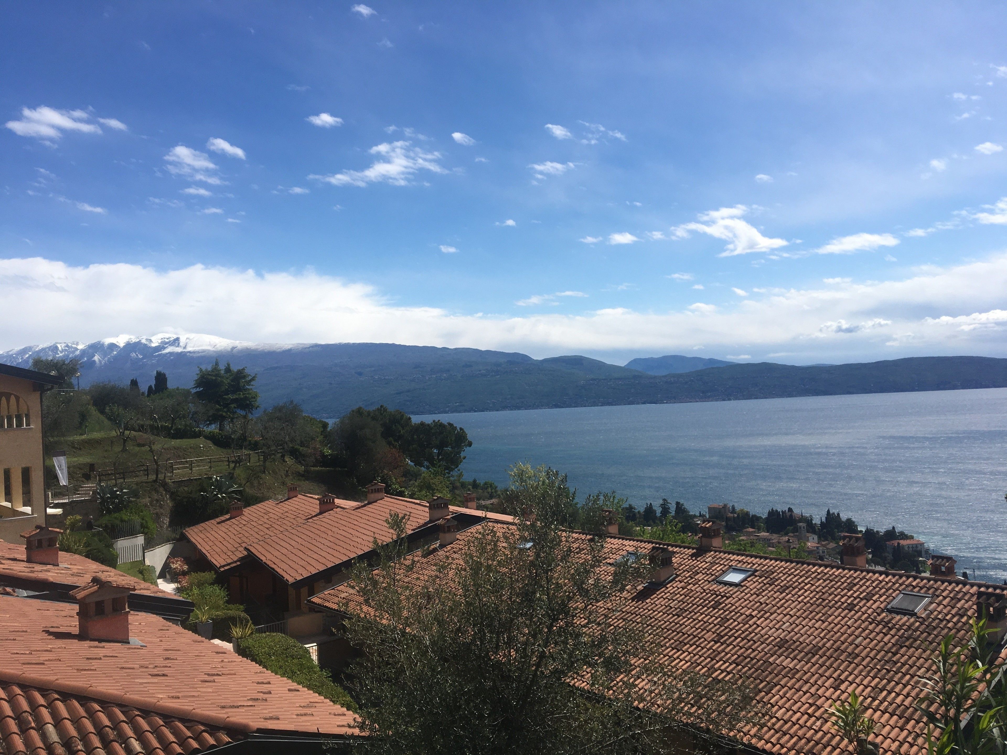 Vista de un lago con montañas al fondo, edificios con tejados de terracota y cielo despejado.