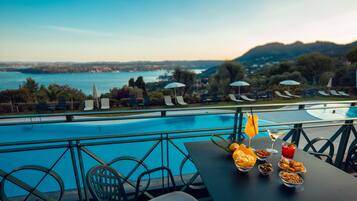 A poolside dining area with a table set for two, overlooking a large pool and a scenic view of a lake and hills.