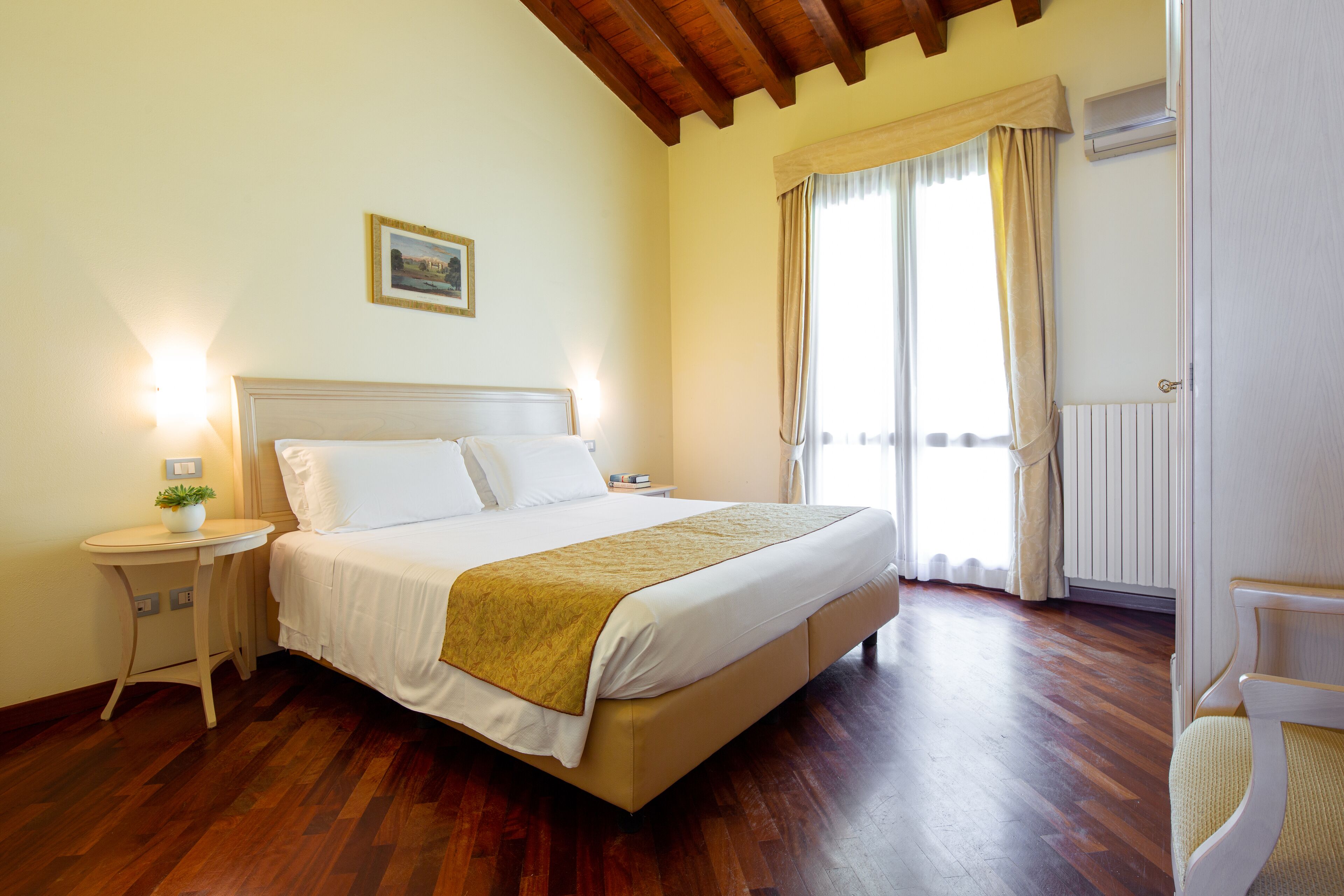 A bedroom with a bed, bedside tables, a nightstand, a window with curtains, and a radiator.