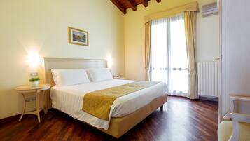 A bedroom with a bed, bedside tables, a nightstand, a window with curtains, and a radiator.