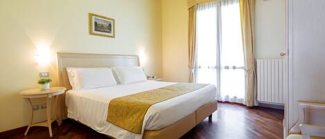 A bedroom with a bed, bedside tables, a nightstand, a window with curtains, and a radiator.