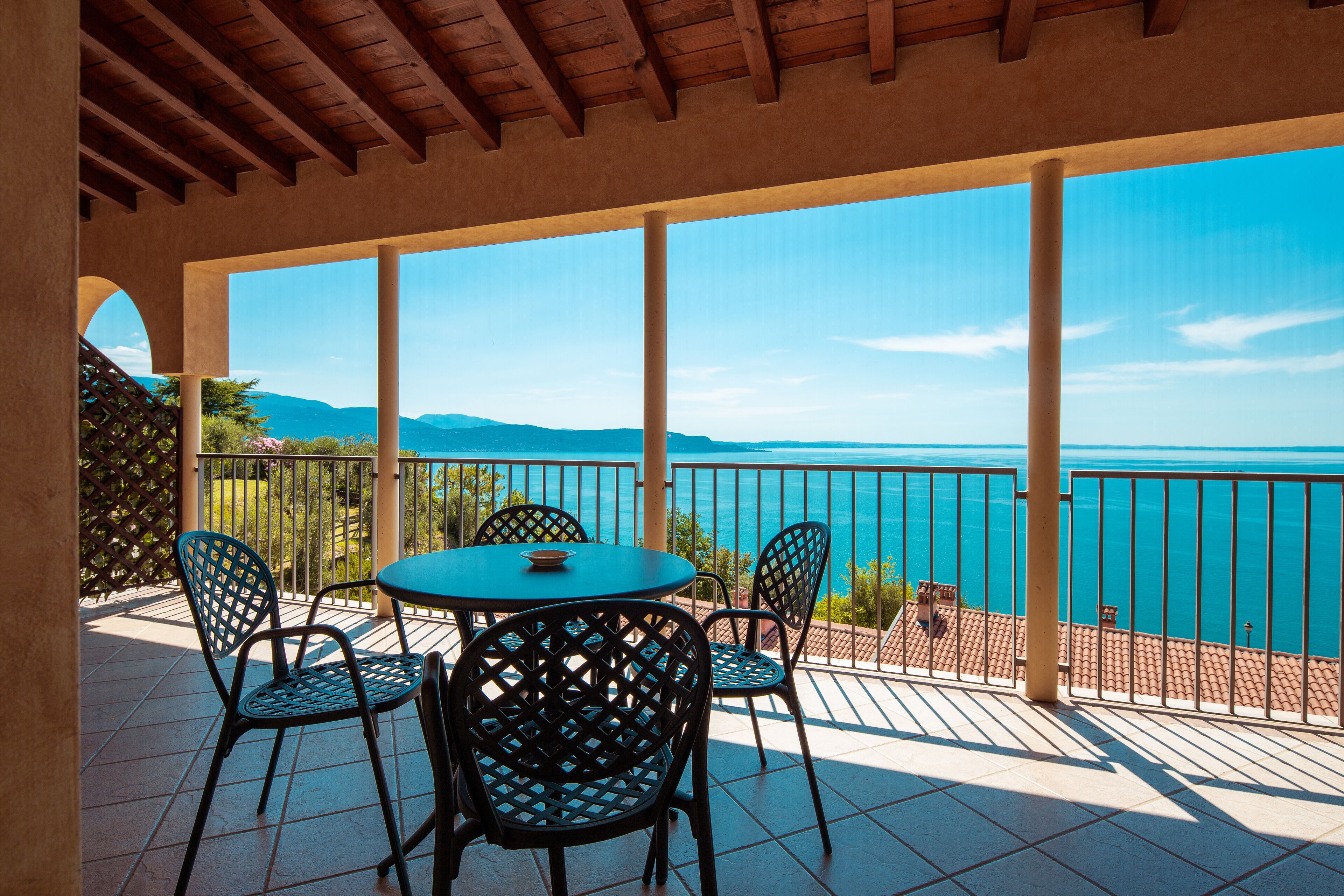 A covered outdoor seating area with a table and chairs, overlooking a body of water and distant mountains.