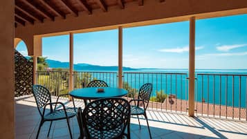 A covered outdoor seating area with a table and chairs, overlooking a body of water and distant mountains.