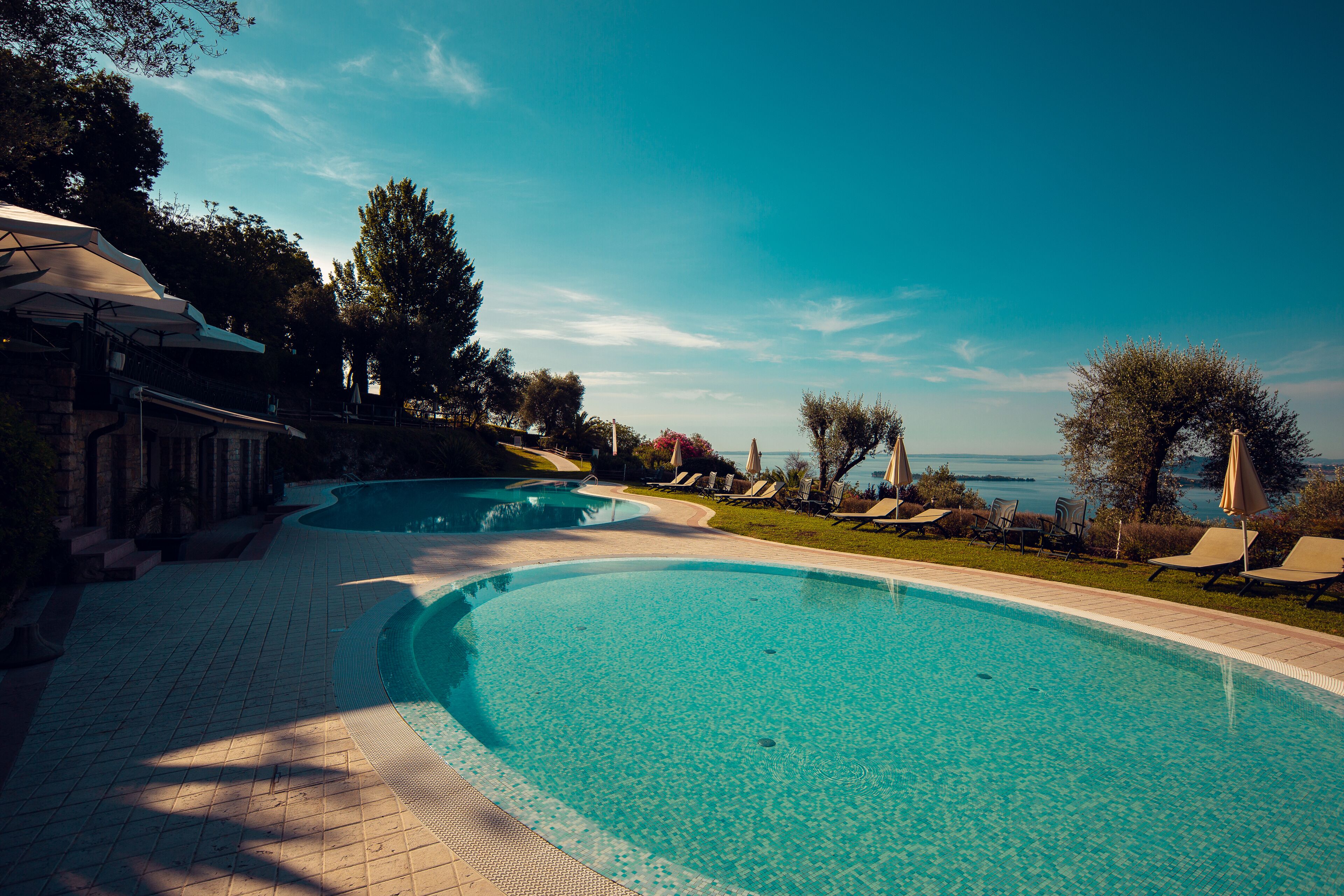 A swimming pool with a curved edge, surrounded by lounge chairs and umbrellas, with a view of the sea in the background.