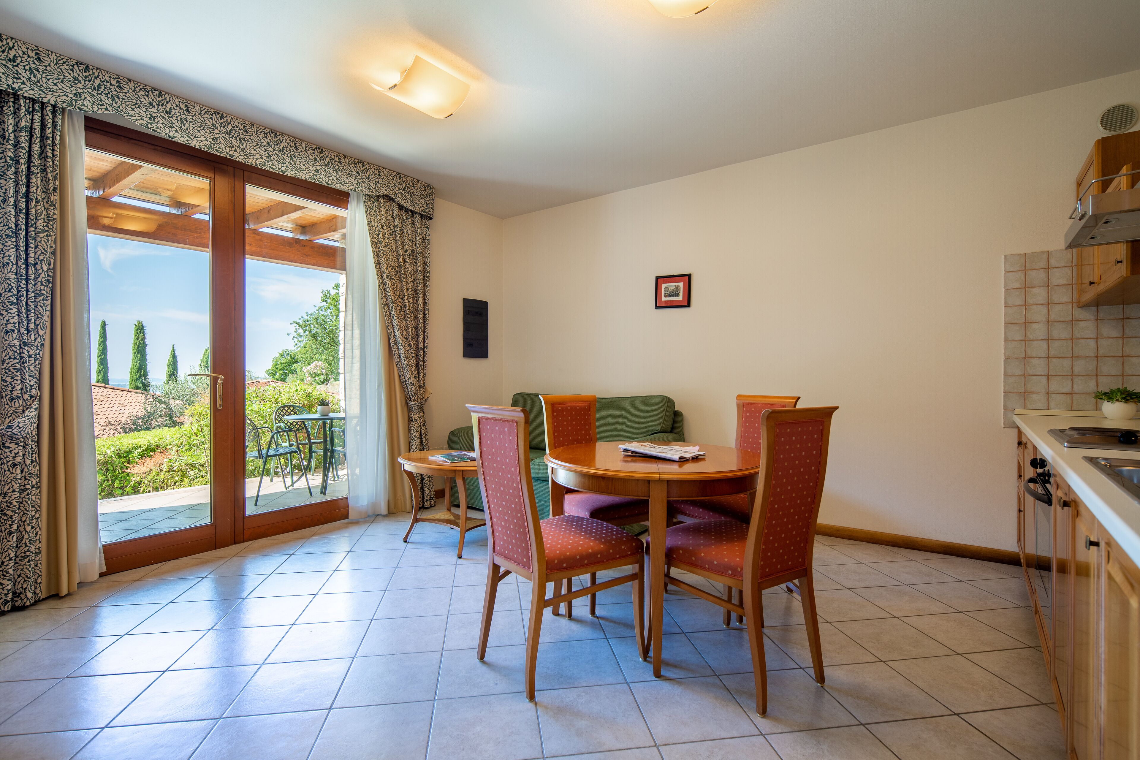 A dining area with a table and chairs, a sofa, and a view through a sliding glass door to the outdoors.