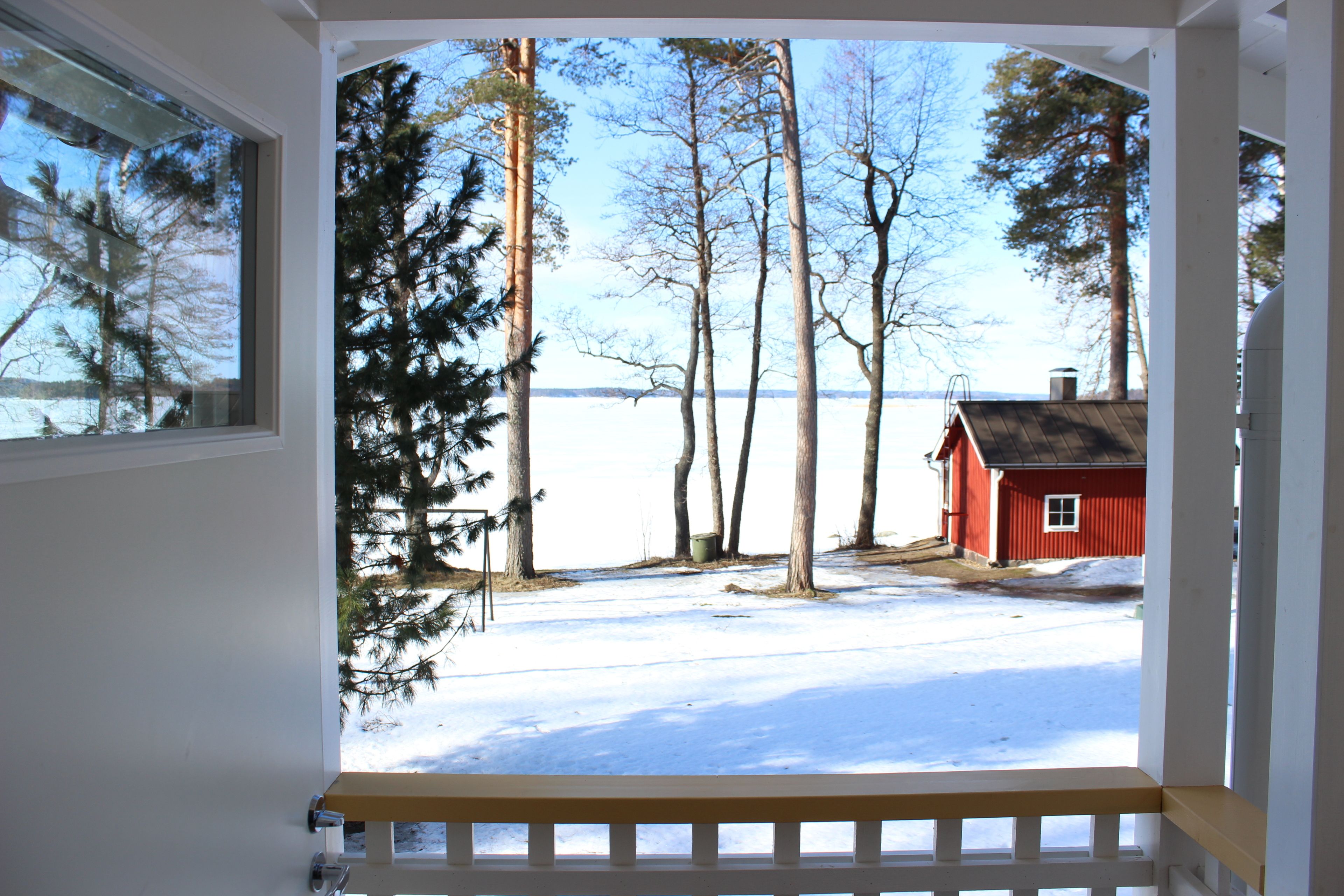 A view from a window overlooking a snowy landscape with a red building and tall trees.