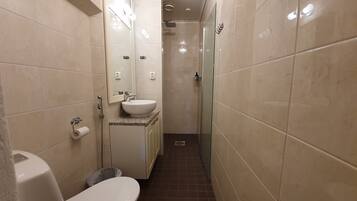 A narrow bathroom with a toilet, sink, and shower.