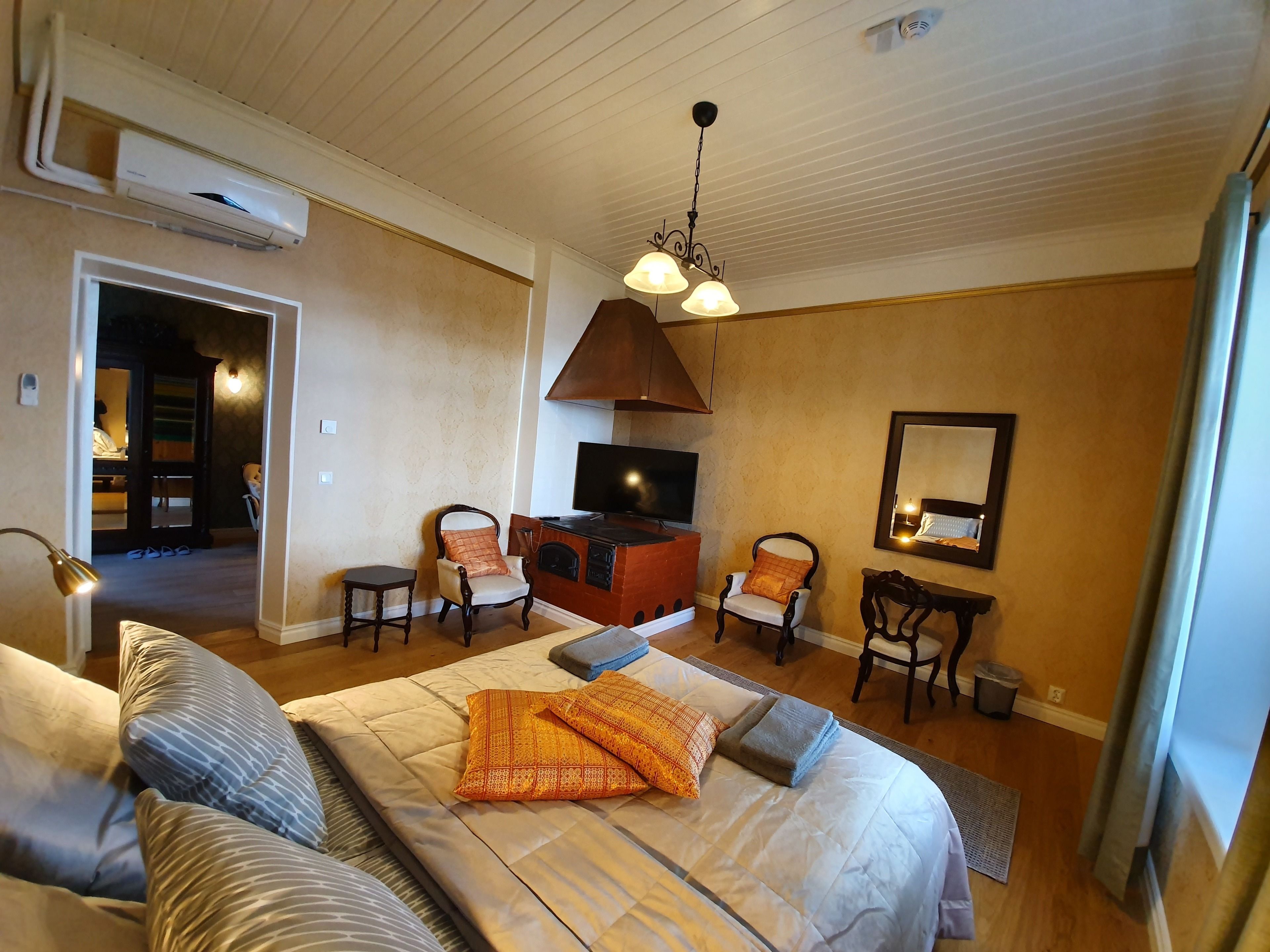 A hotel room with a large bed, two armchairs, a TV, a fireplace, and a mirror.