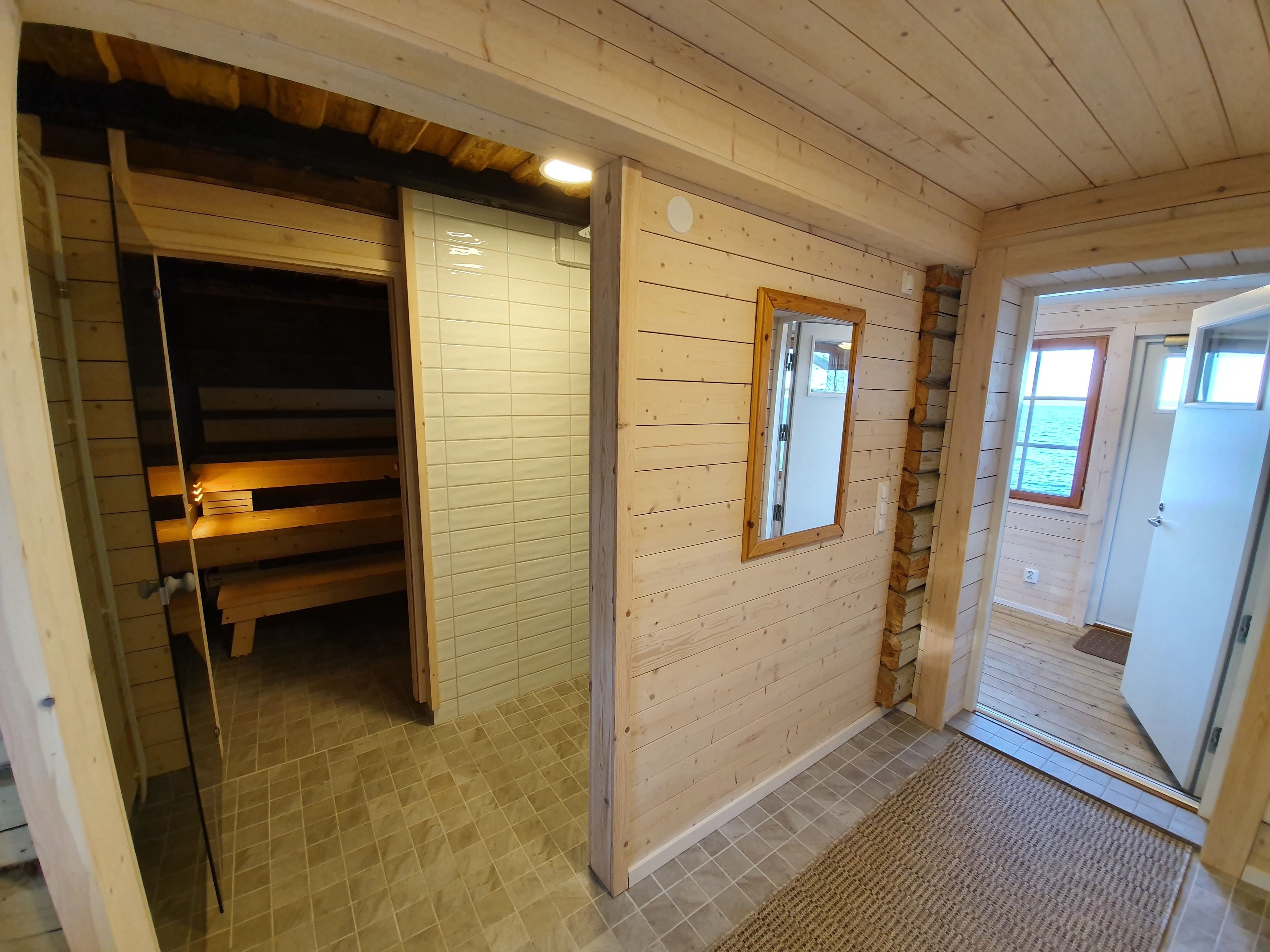 A wooden interior with a bench, a door, and a mirror on the wall.