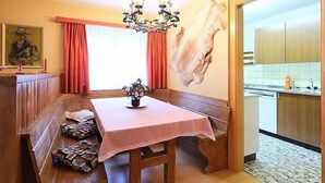A dining area with a wooden bench, a table with a pink tablecloth, a chandelier, and a large fur piece on the wall.