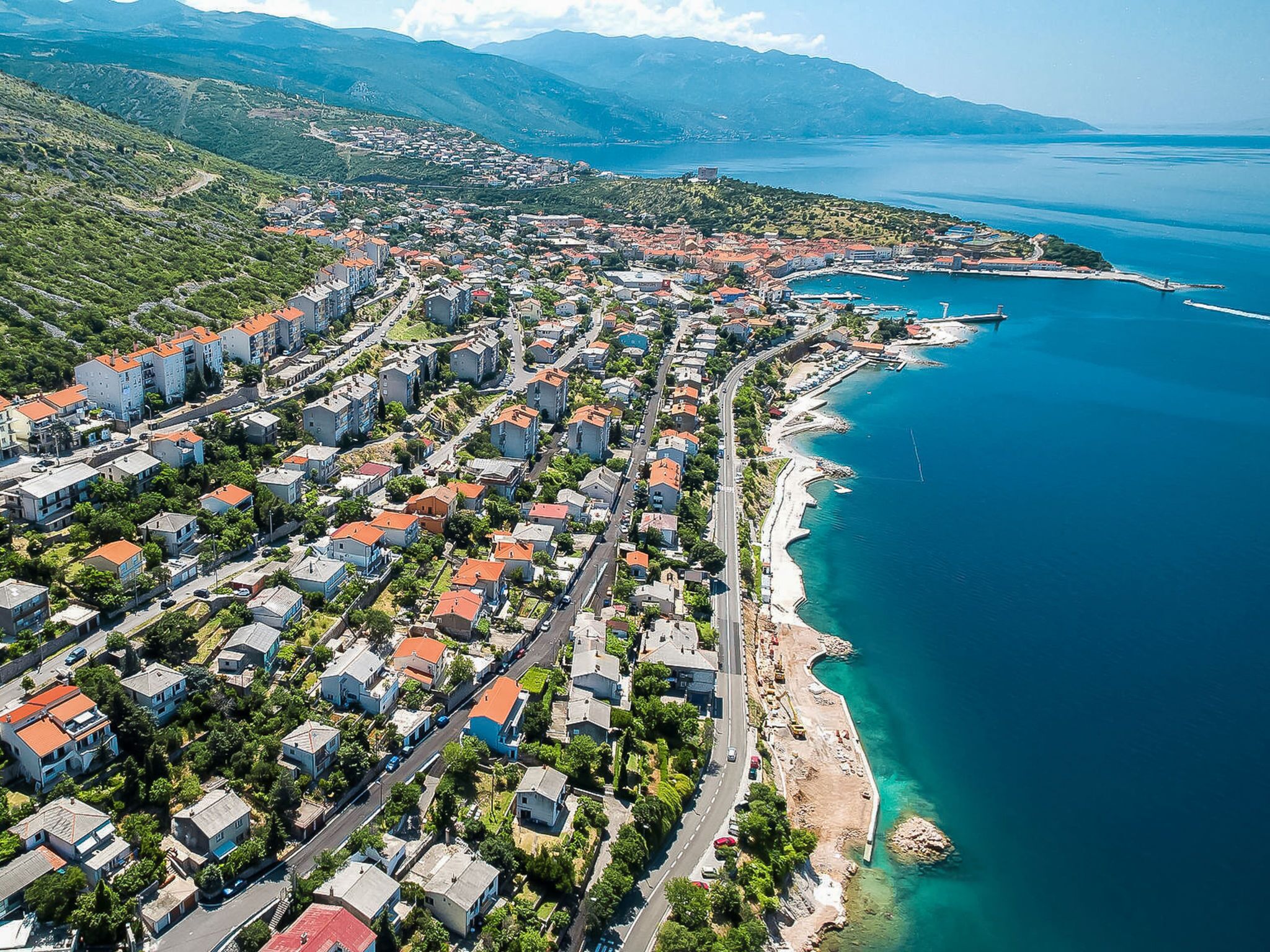 An aerial view of a coastal town with residential buildings, a road, and a marina.