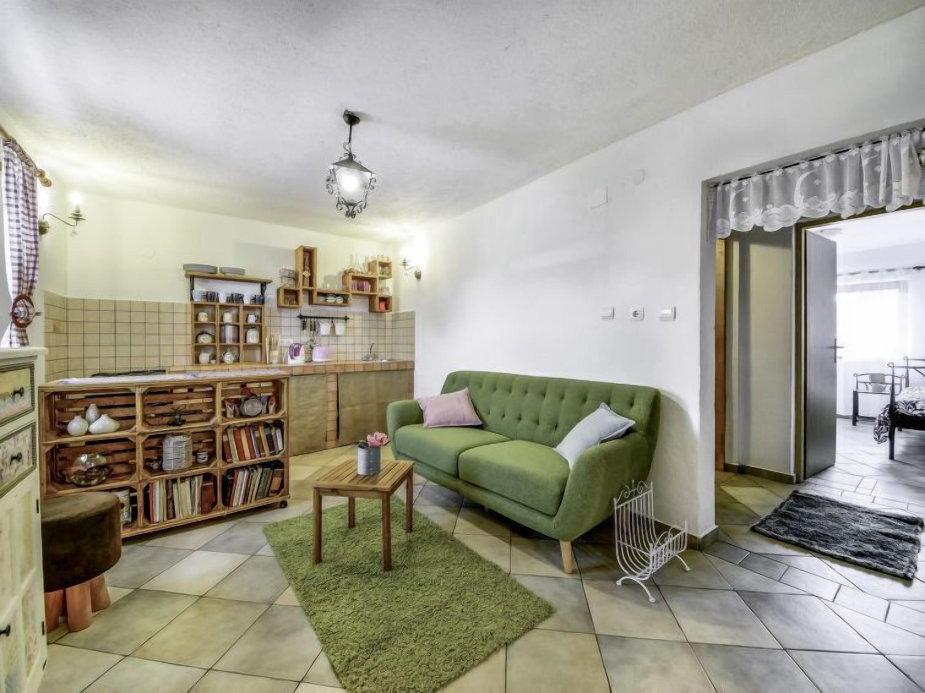 Un salon chaleureux avec un canapé vert, une bibliothèque en bois et un coin cuisine aux murs carrelés et aux meubles de rangement en bois.