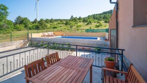 Ein Balkon mit Holztisch und Stühlen, ein Schwimmbad und im Hintergrund ein Windrad.