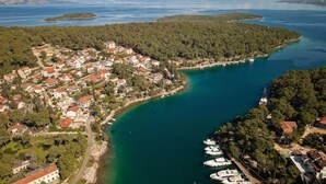 Vue aérienne d’une ville côtière dotée d’un port de plaisance, entourée de forêts denses et bordée d’eaux d’un bleu limpide.