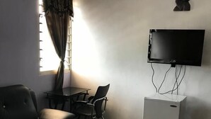 A room with a sofa, a small table, a TV mounted on the wall, and a refrigerator. - Mace Lodge (Sekondi-Takoradi)