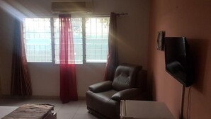 A room with a leather chair, a flat-screen TV mounted on the wall, a window with curtains, and a tiled floor. - Mace Lodge (Sekondi-Takoradi)