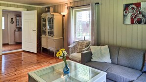 Un salon comprenant une table basse avec un plateau en verre, un canapé gris, un fauteuil en osier et un meuble avec des portes en verre.