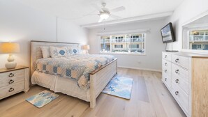 A bedroom with a bed, a nightstand, a dresser, a ceiling fan, a window with a view, and a TV on the dresser.