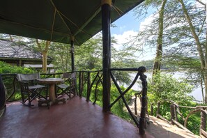 Un espace extérieur aménagé, abrité et doté de tables et de chaises, offrant une vue sur une étendue d’eau et une végétation luxuriante.