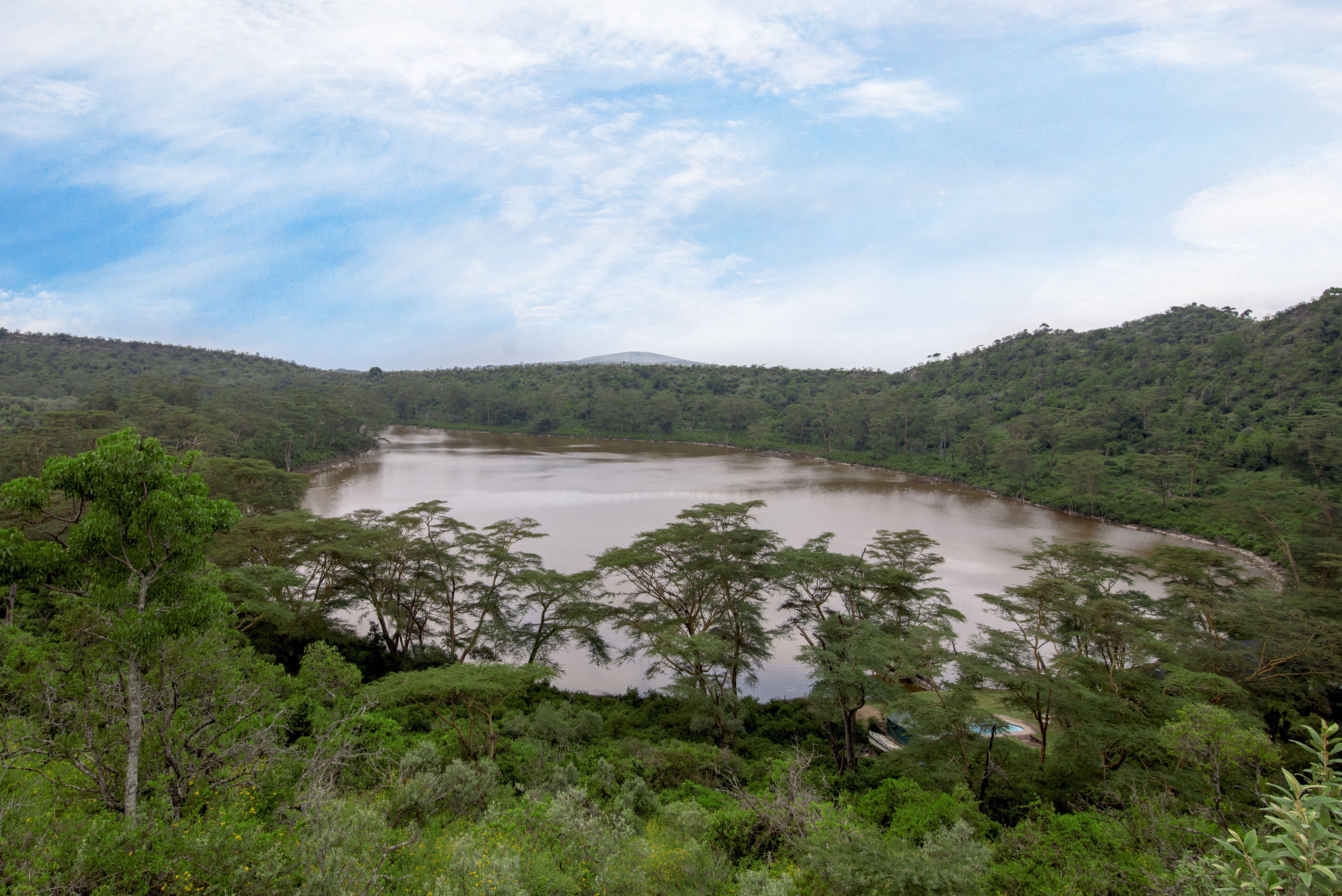 Paisatge natural amb un llac envoltat de vegetació densa i turons.