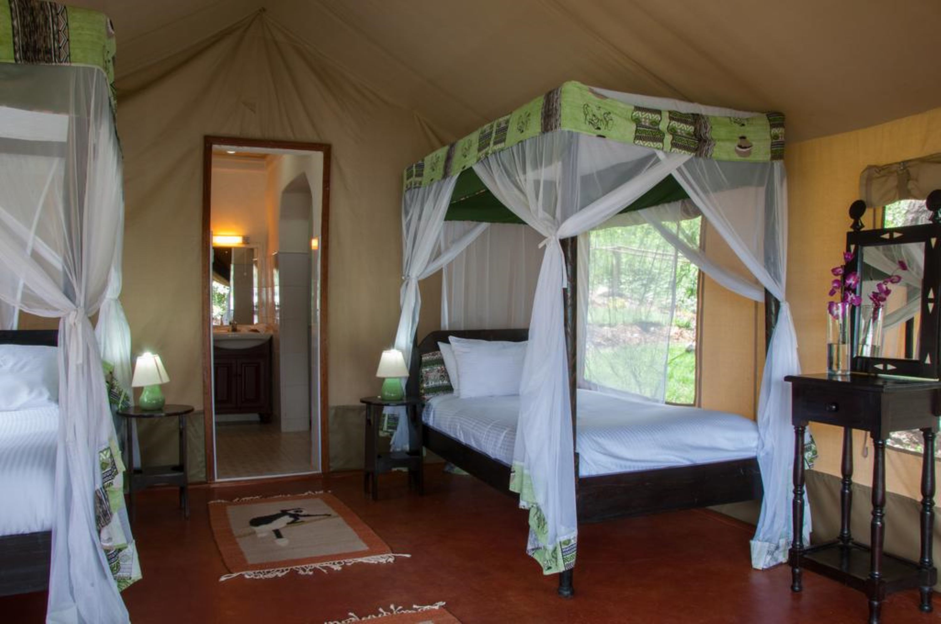 A tent-style room with two beds, each with a canopy, a small table, and a mirror.