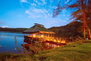 Una terraza de madera con zona de estar cubierta, con vistas a un lago tranquilo, rodeada de árboles.