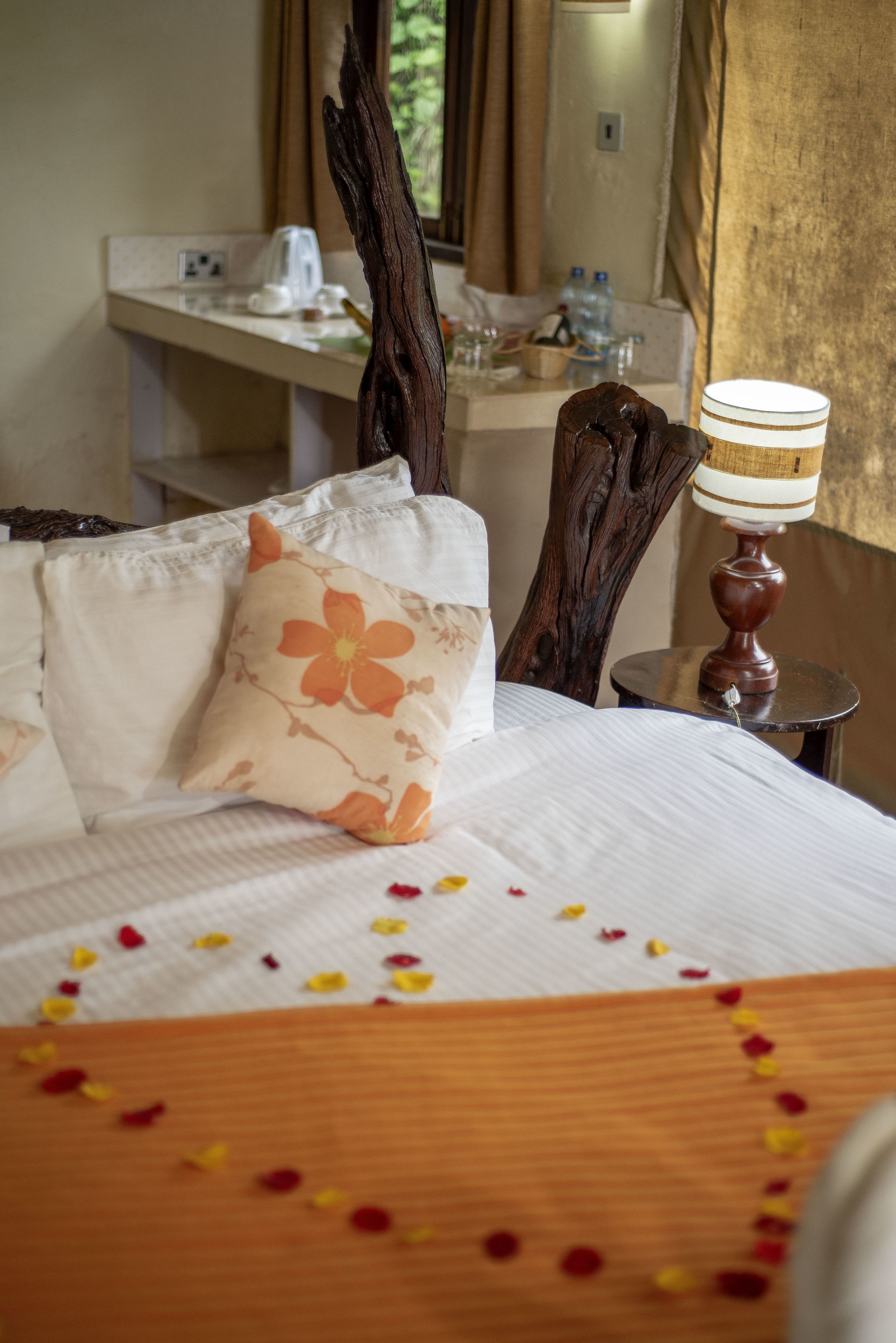 Habitación de hotel con cama, cabecera de madera, mesita de noche con lámpara y ventana con cortinas.