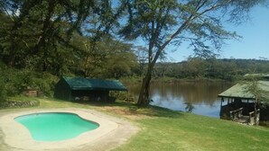 Una piscina con sillas de descanso, un cobertizo pequeño y vista a un lago.
