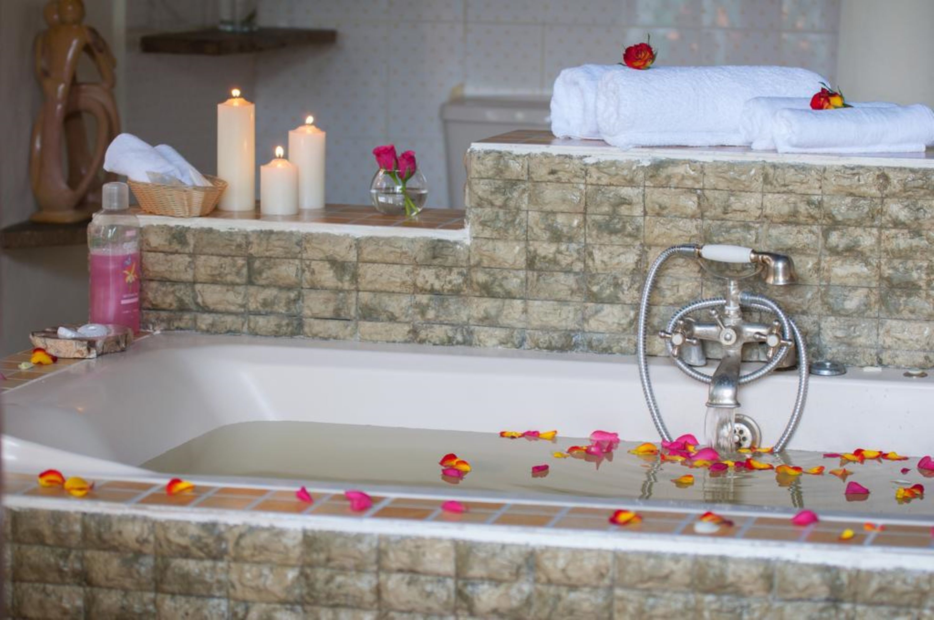 A bathtub with rose petals, candles, and towels.