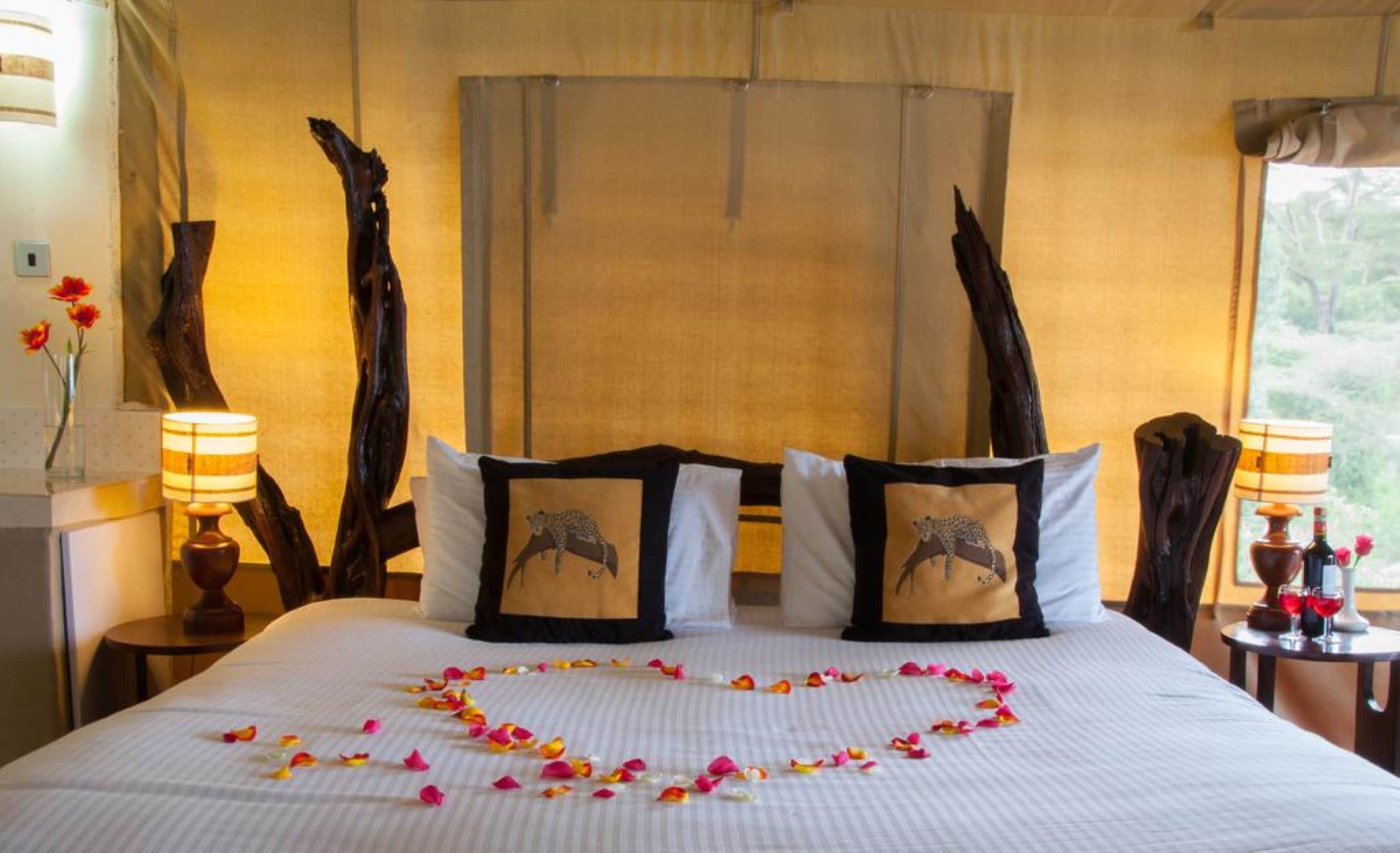 A hotel room with a large bed, two nightstands, a window with curtains, and a view of greenery outside.