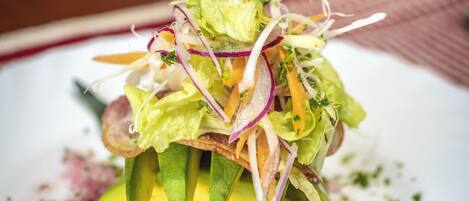 Un plato con ensalada, rebanadas de aguacate y un aderezo cremoso.