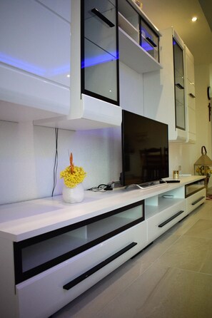 Enjoy a stylish living space with a flat-screen TV, comfortable seating, and a beautiful vase with fresh flowers.
