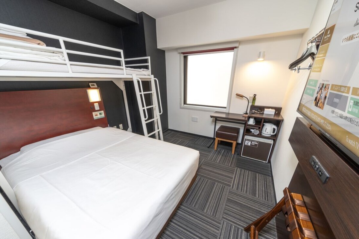 Een hotelkamer met een stapelbed, bureau, stoel en een televisie.