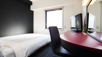 A hotel room with a bed, a desk with a computer, a chair, and a window with a view.