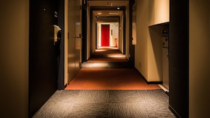 A hotel hallway with carpeted floors, doors on both sides, and a red door at the end. - Super Hotel Tokyo Akabane-Eki Higashiguchi Ichibangai (Tokyo)