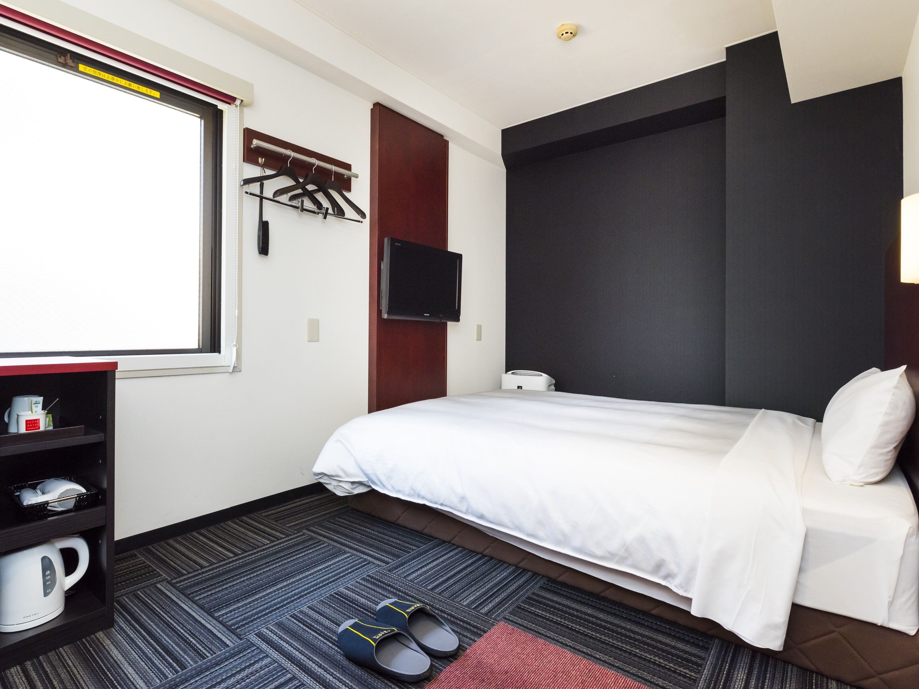 A hotel room with a bed, a TV mounted on the wall, a coffee machine, and a shoe rack.