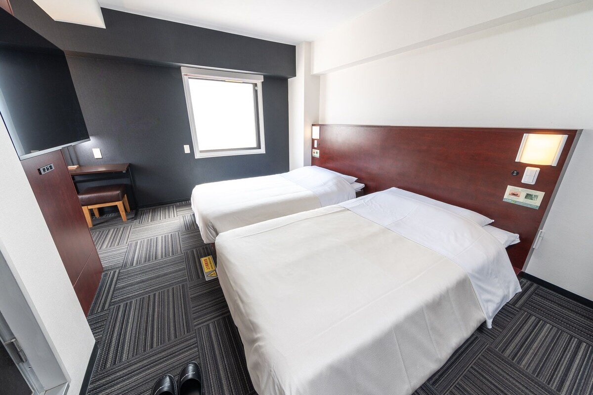 Een hotelkamer met twee bedden, een bureau, een stoel, een televisie en een raam.