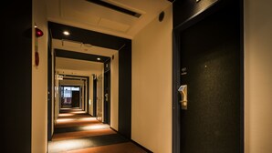A hotel hallway with carpeted floors, a dark door on the right, and a lighted corridor leading to a room. - Super Hotel Tokyo Akabane-Eki Higashiguchi Ichibangai (Tokyo)