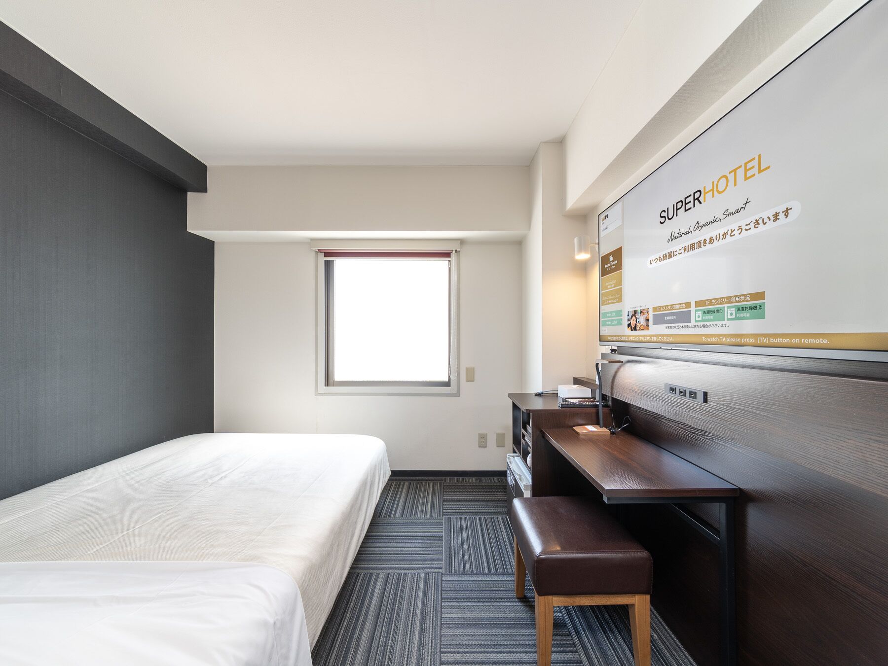 A hotel room with a bed, a desk, a chair, a TV, and a window.