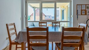 A dining area with a table and chairs, a view through a glass door to the outside, and a bulletin board with notices. - Ferienwohnungen beim Europapark Rust (Rust)