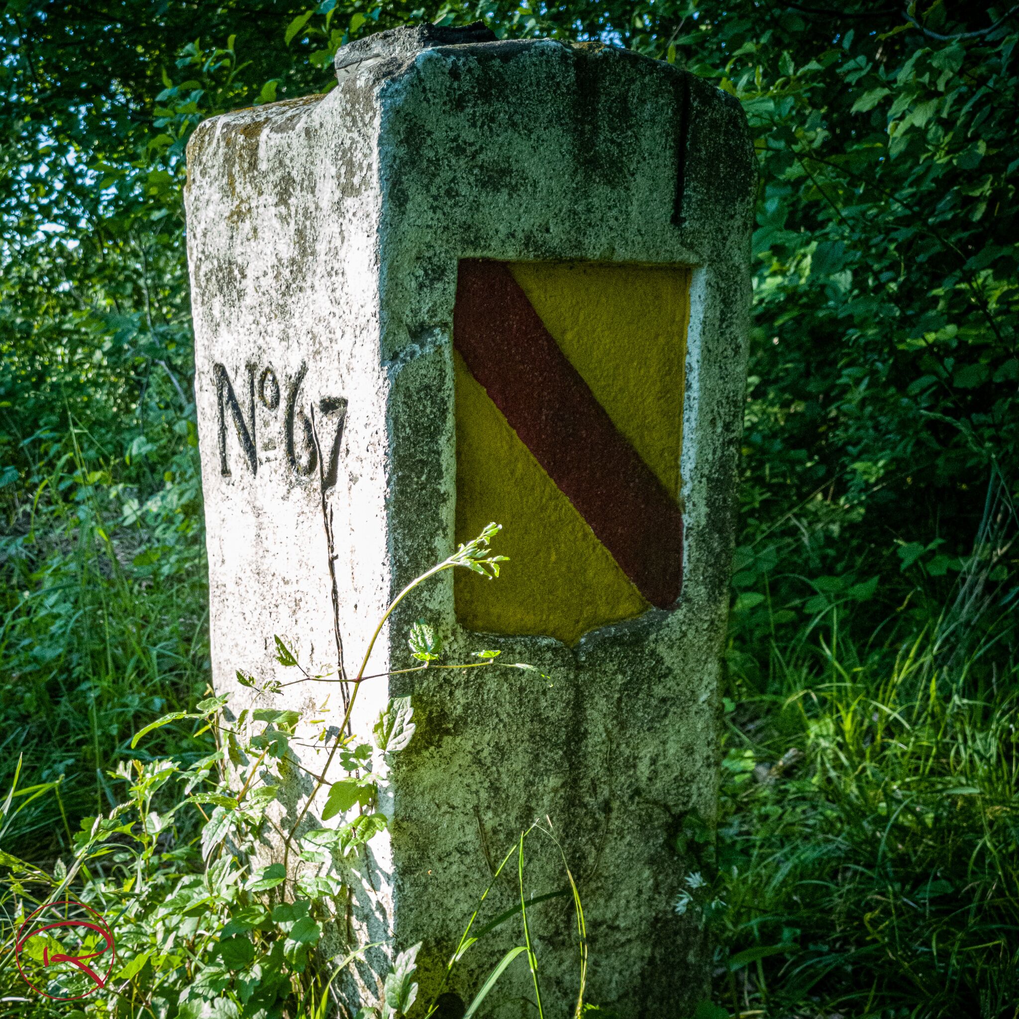 A weathered stone marker with a yellow and red diagonal stripe, labeled "N67" in the center.