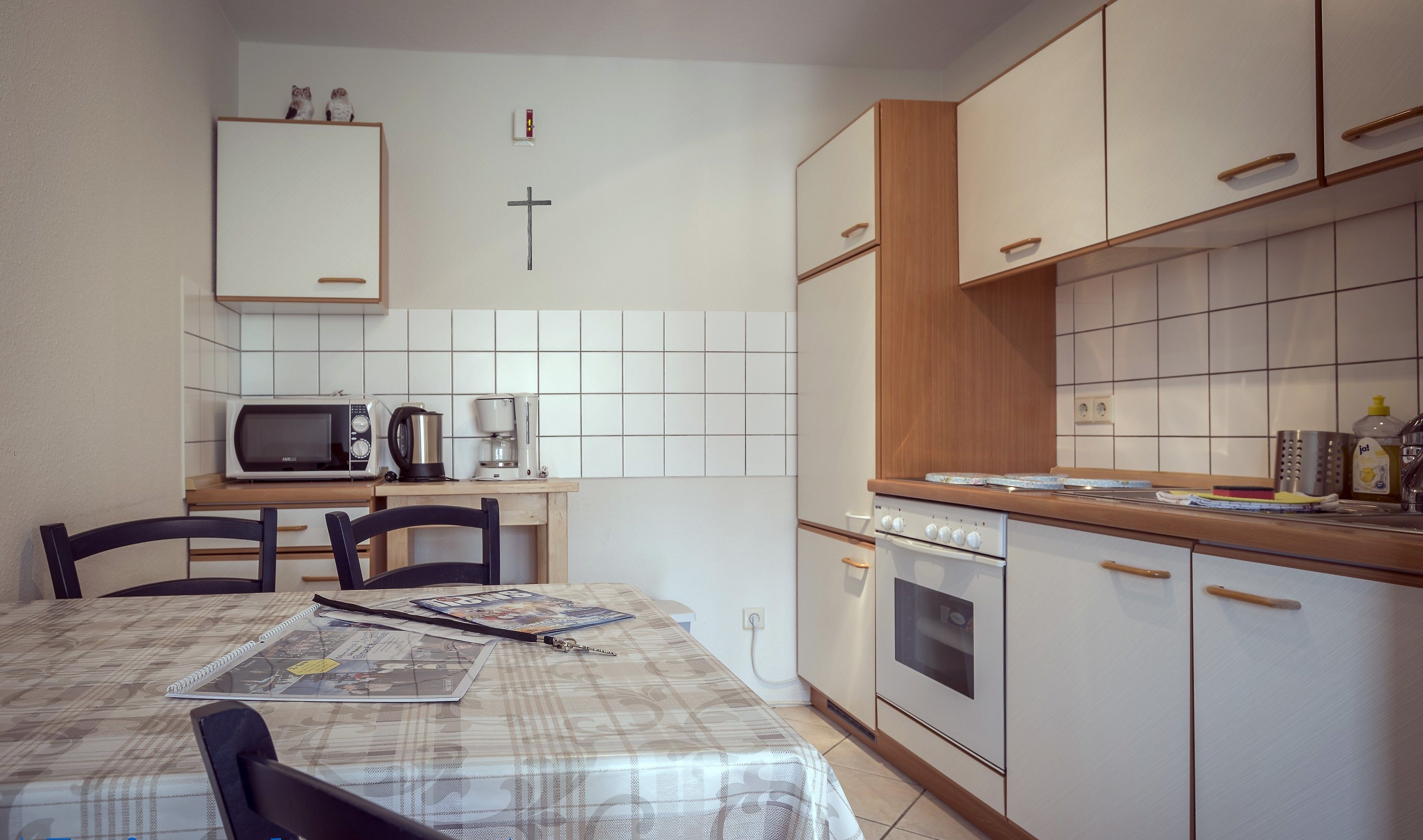A compact kitchen with a microwave, coffee maker, and oven. There is a table with a placemat and a chair.