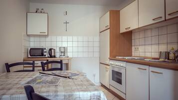 A compact kitchen with a microwave, coffee maker, and oven. There is a table with a placemat and a chair.