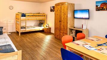 A room with bunk beds, a wooden wardrobe, a television, and a dining table with chairs.