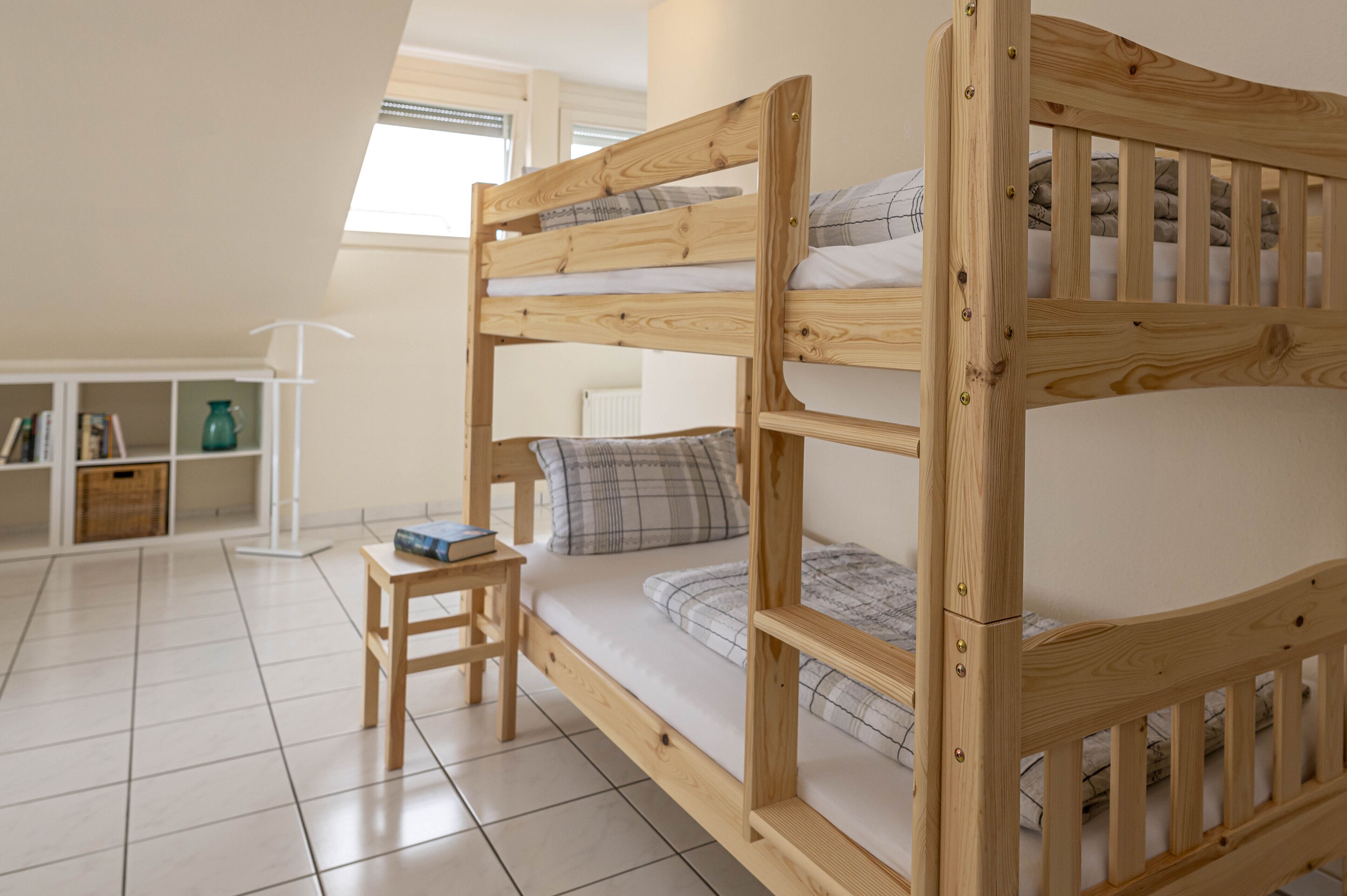 Une chambre avec un lit superposé, une petite table en bois et une étagère avec des livres et un vase.