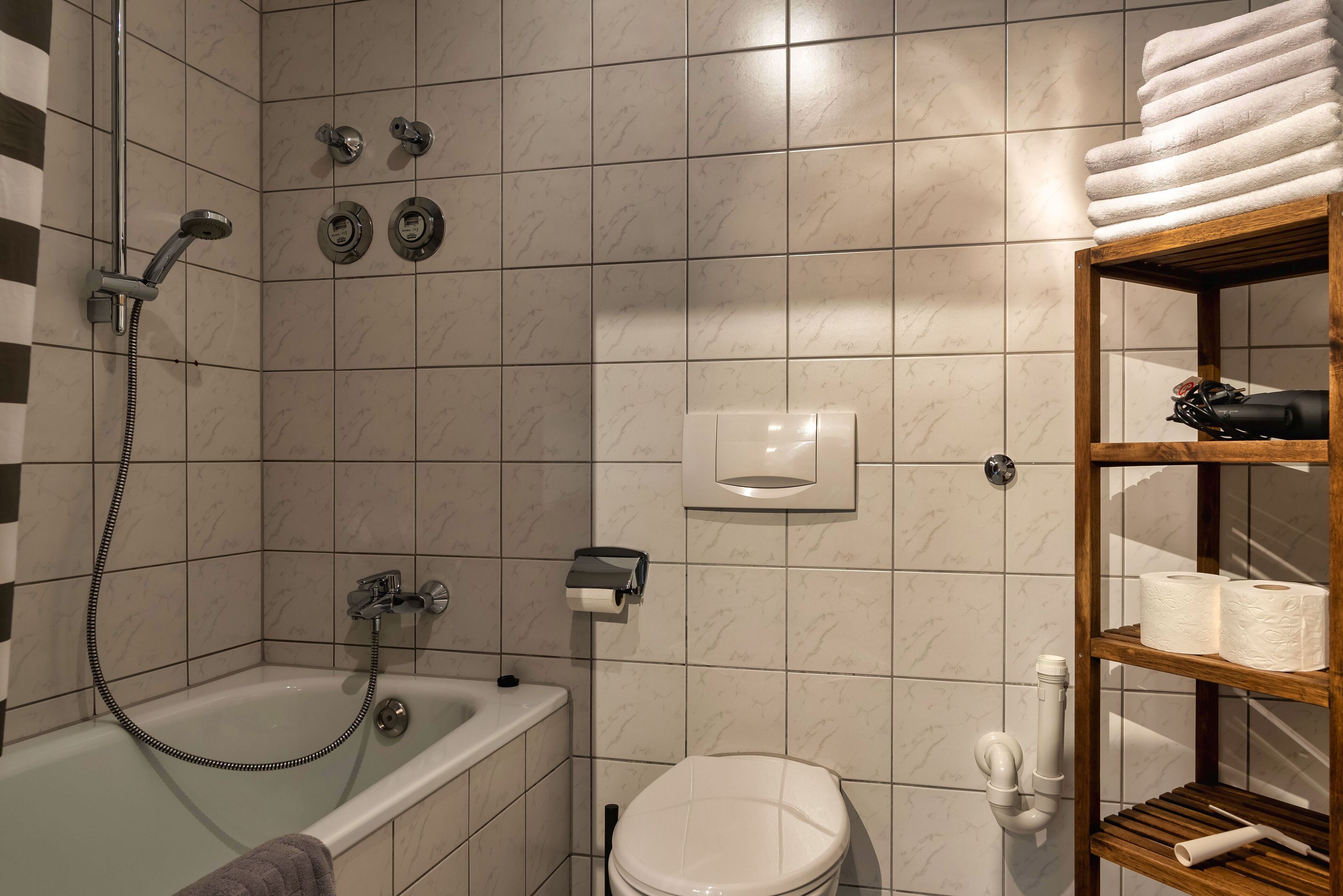 Un baño con bañera, inodoro y repisa con toallas y artículos de aseo.