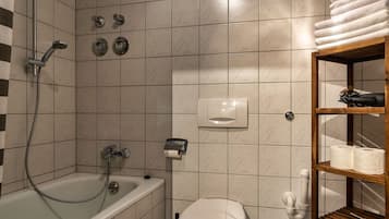 Un baño con bañera, inodoro y repisa con toallas y artículos de aseo.
