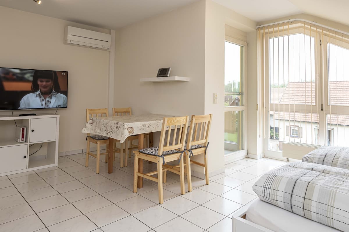 A modern living room with a dining area, a TV, and a balcony with a view.