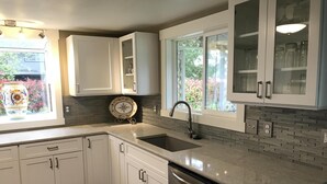 Uma cozinha moderna com armários brancos, lava-louças de aço inoxidável e uma janela ampla com vista para o verde.
